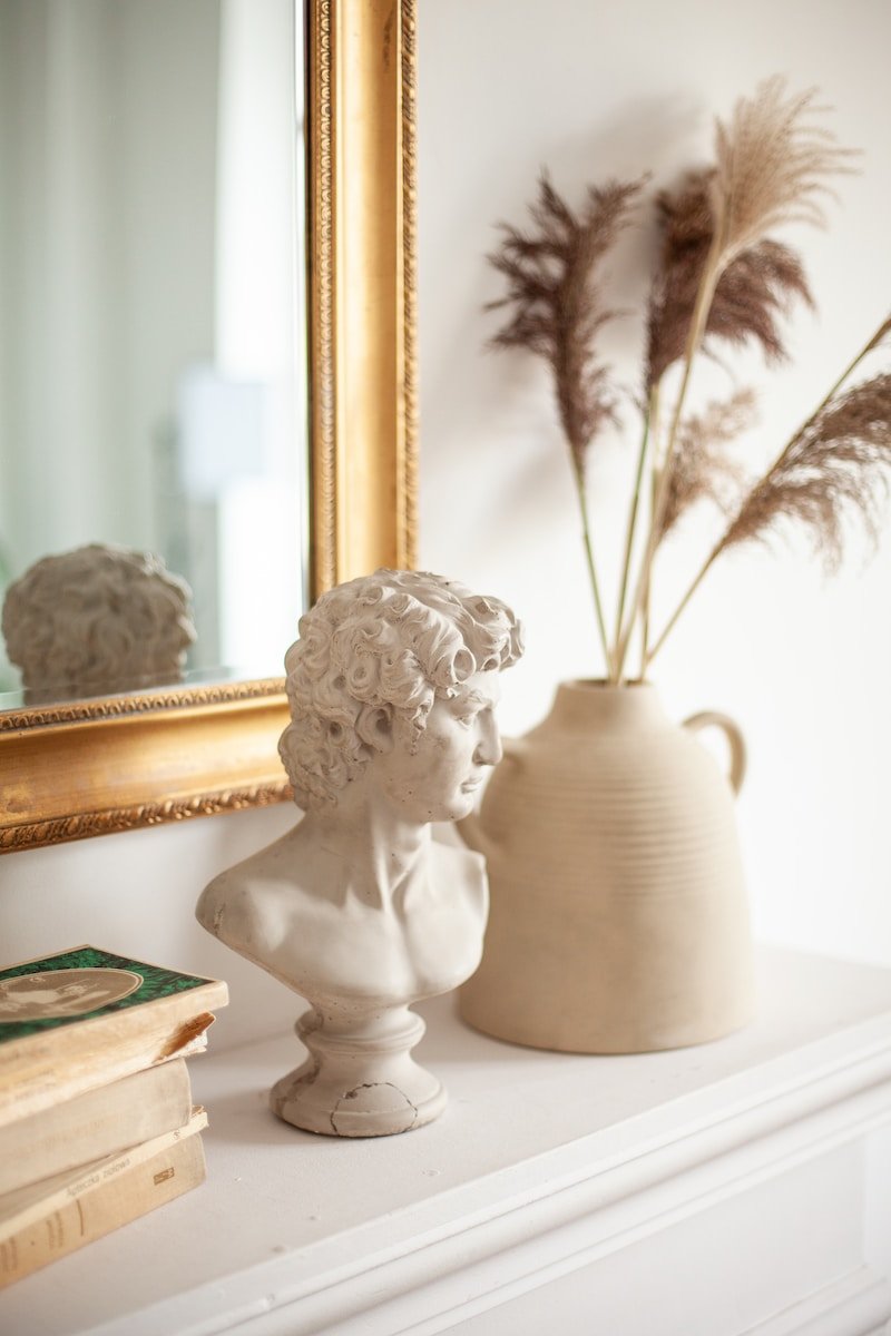 Photo by Katie Luka a white vase with a plant in it next to a mirror